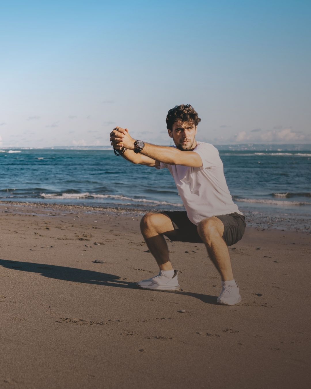 Man doet een squat op het strand met de zee op de achtergrond